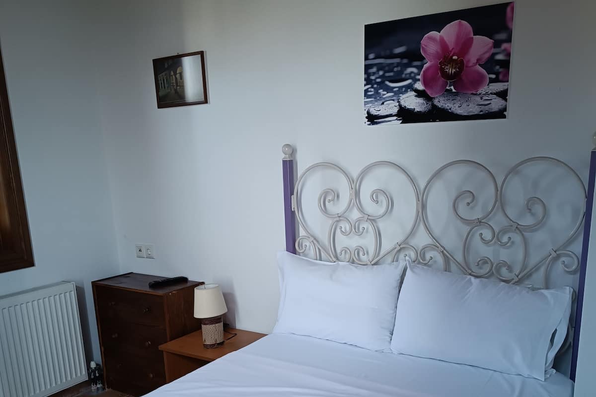 A neatly made bed with white linens, a decorative headboard, and a wall-mounted picture of a pink flower.