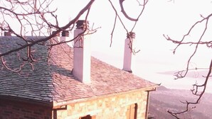 Um edifício de pedra com telhado inclinado, duas janelas visíveis e uma chaminé.