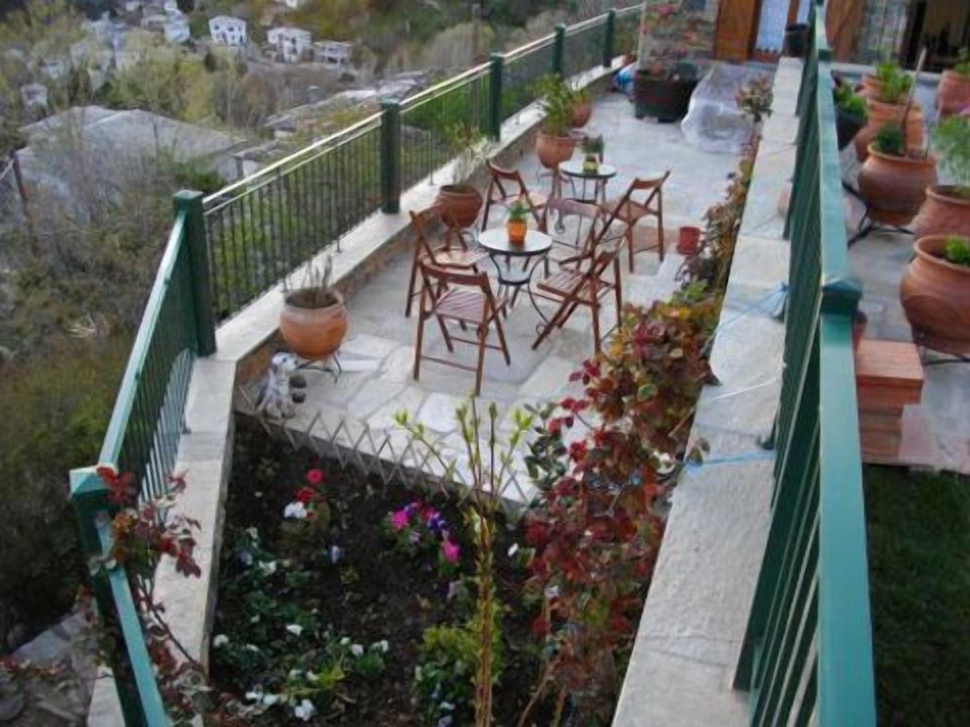 Un balcón con mobiliario exterior, plantas en macetas y un sendero de piedra.