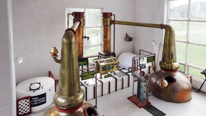 Uma destilaria com grandes alambiques de cobre, vigas de madeira e uma grande janela que permite a entrada de luz natural.