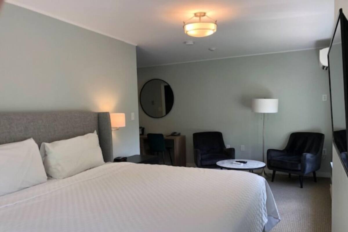 Ein Hotelzimmer mit einem großen Bett, einem Schreibtisch, zwei Stühlen, einem runden Tisch, einem Spiegel und einer Deckenleuchte.
