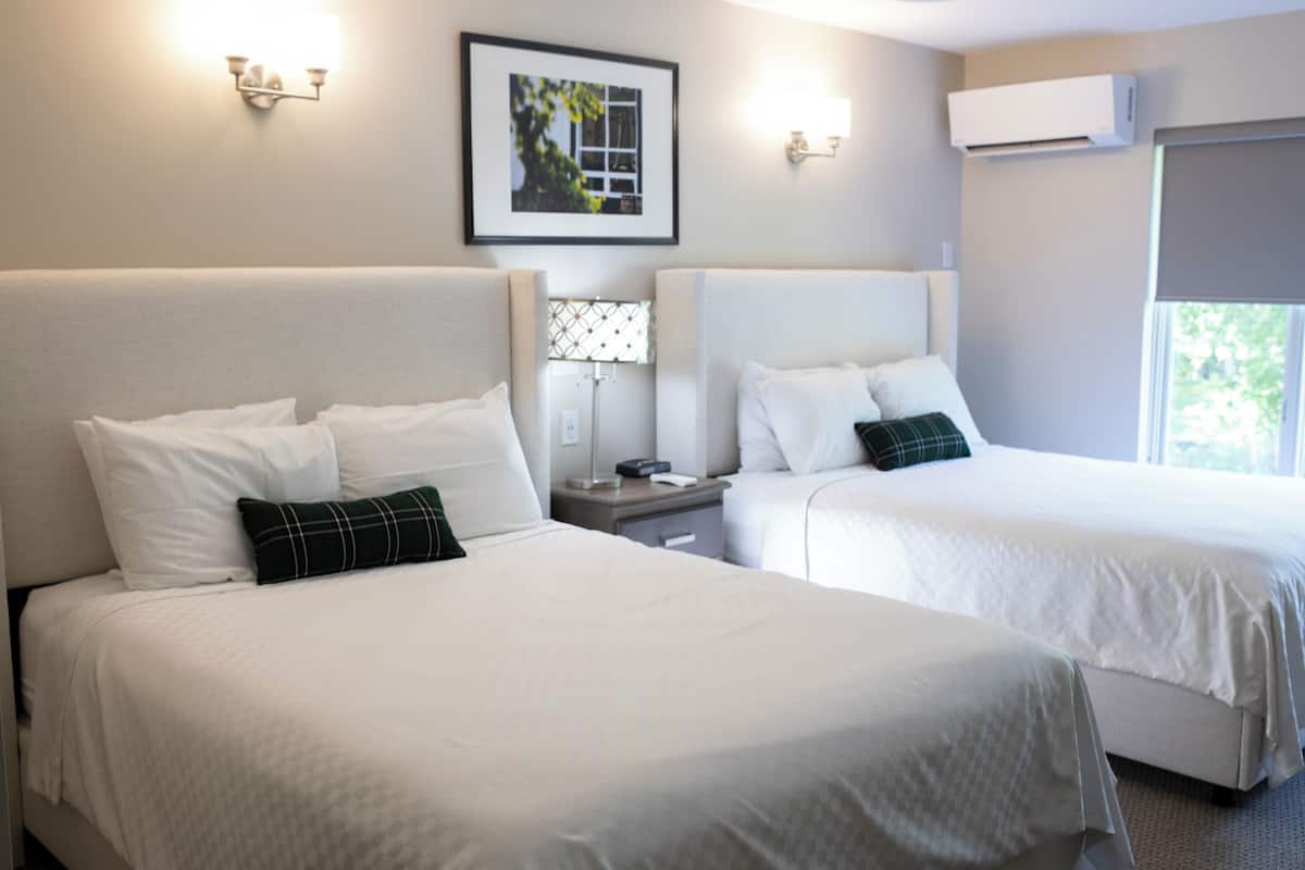 Ein Hotelzimmer mit zwei Betten, einem Nachttisch, einer Lampe und einem gerahmten Bild an der Wand.