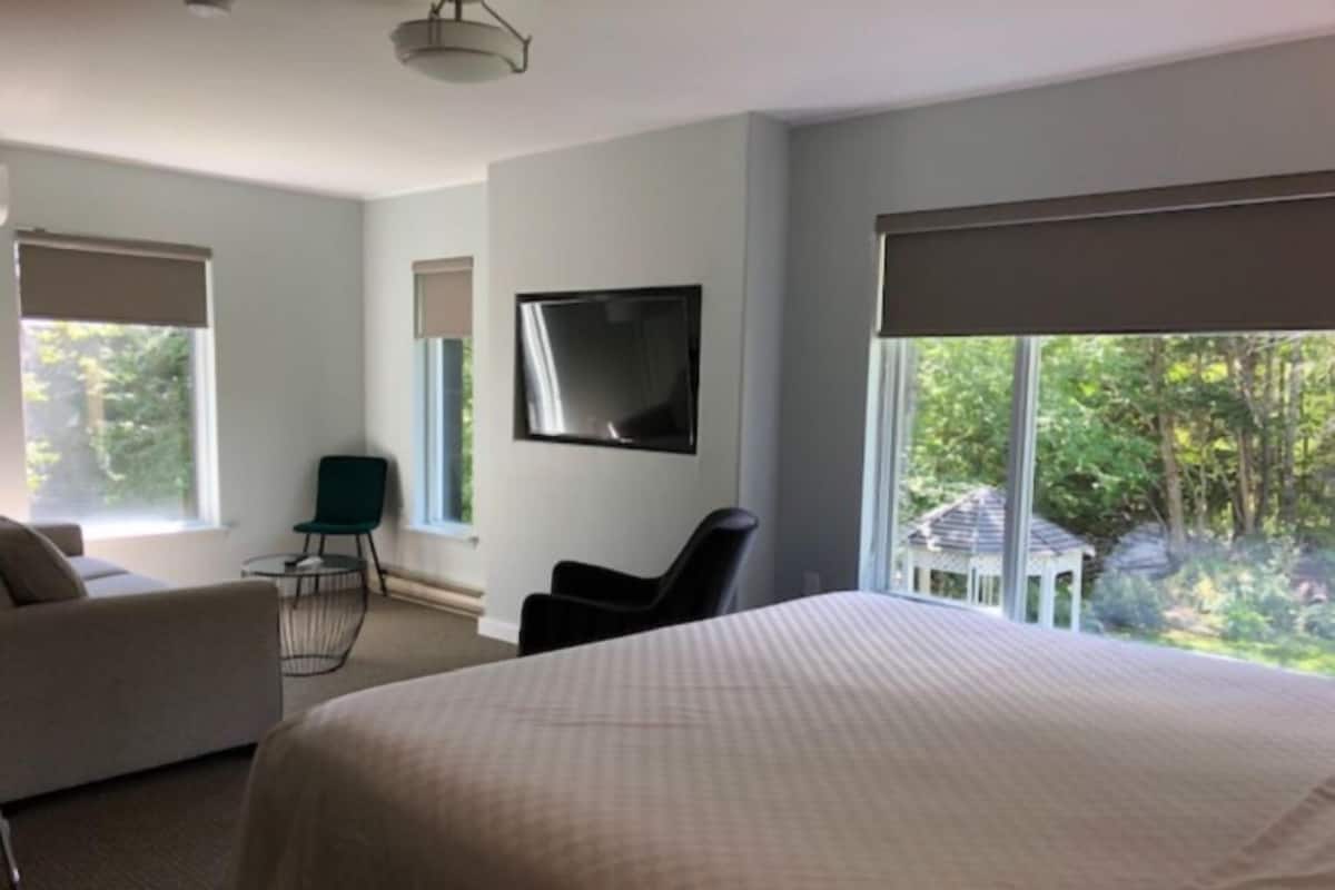 Ein modernes Hotelzimmer mit einem großen Bett, einem Flachbildfernseher, einem Schreibtisch und einem Sessel.