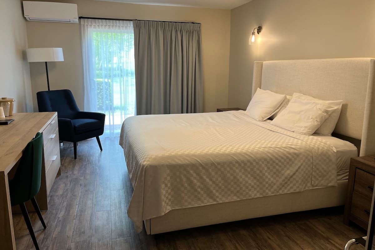 Ein Hotelzimmer mit einem großen Bett, einem Schreibtisch mit Stuhl, einer Lampe und einem Fenster mit Vorhängen.