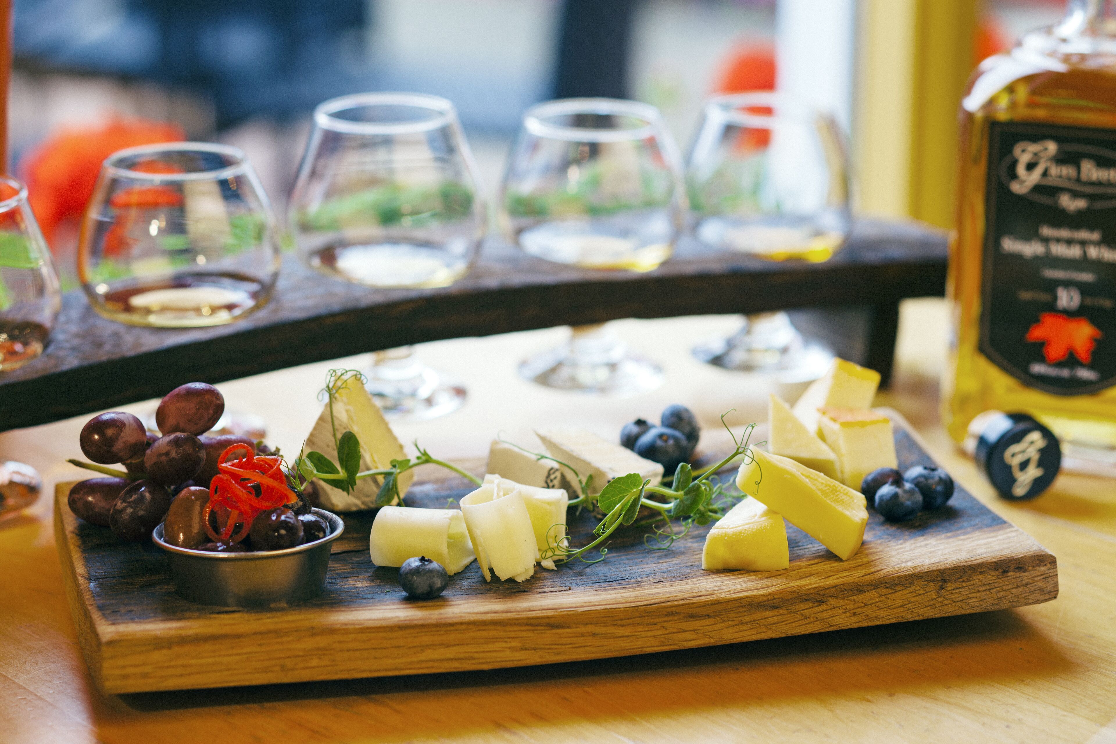 A wooden board with cheese, grapes, and blueberries, and a bottle of wine in the background.