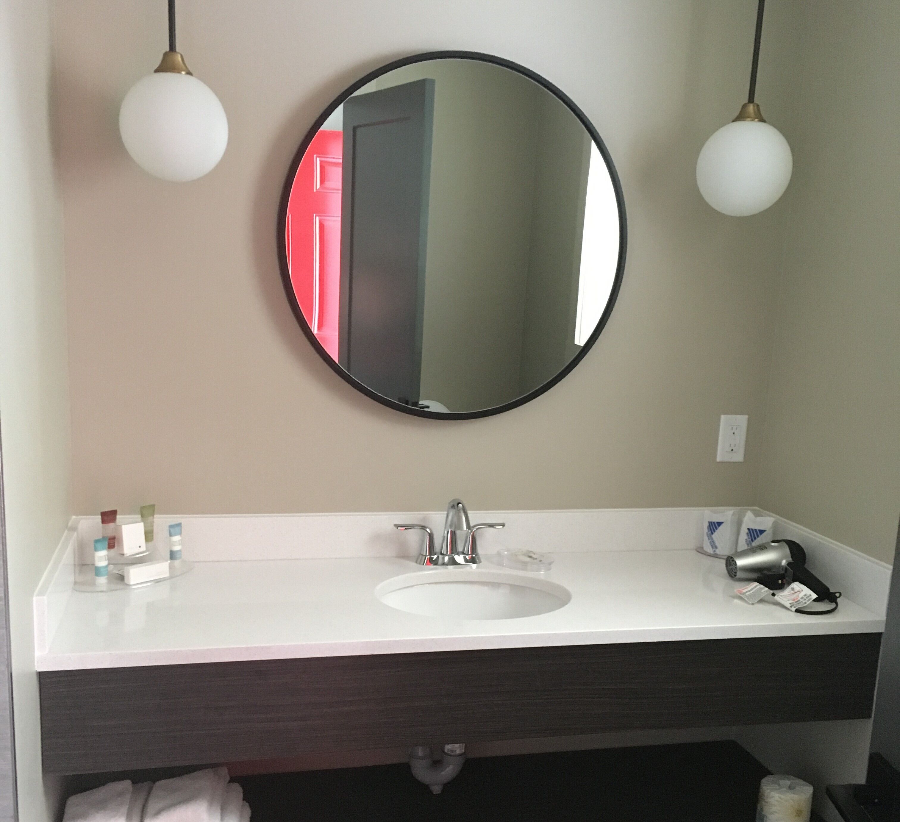 Une salle de bain avec un miroir rond, un lavabo blanc et deux lampes suspendues.