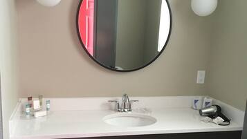 Une salle de bain avec un miroir rond, un lavabo blanc et deux lampes suspendues.