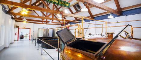 Un vaste espace industriel au décor sobre, avec des poutres en bois apparentes, de grandes cuves en cuivre et une enseigne indiquant « MASH HOUSE ».