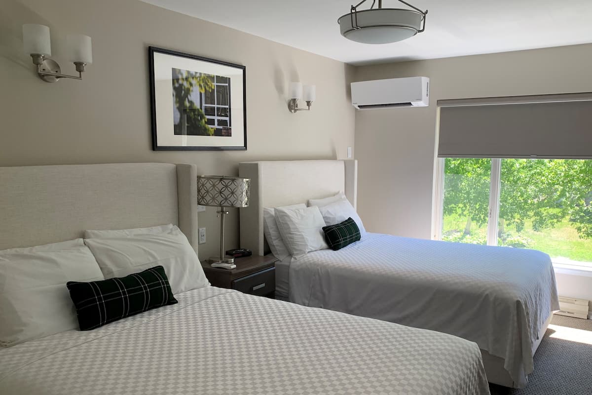 Ein Hotelzimmer mit zwei Betten, einem gerahmten Bild an der Wand, einer Lampe und einer Klimaanlage.