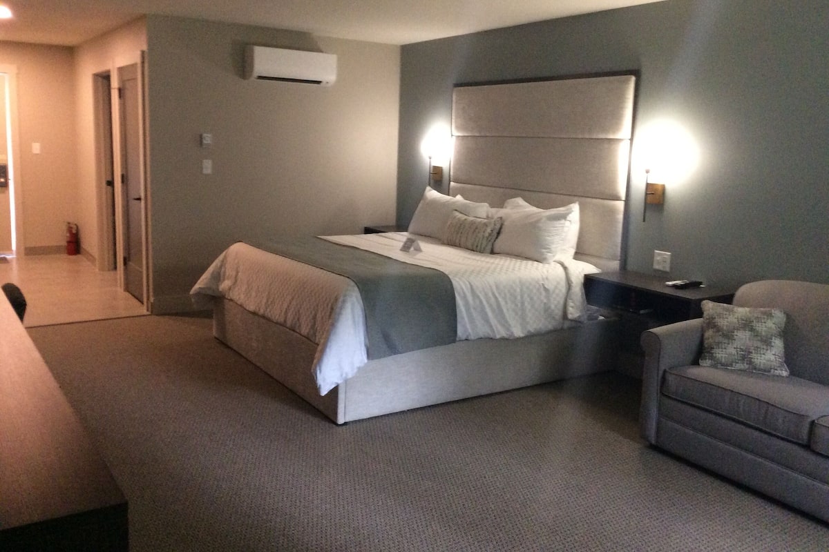 Ein Hotelzimmer mit einem Bett, Nachttischen, einem Sessel und einer Wand-Klimaanlage.