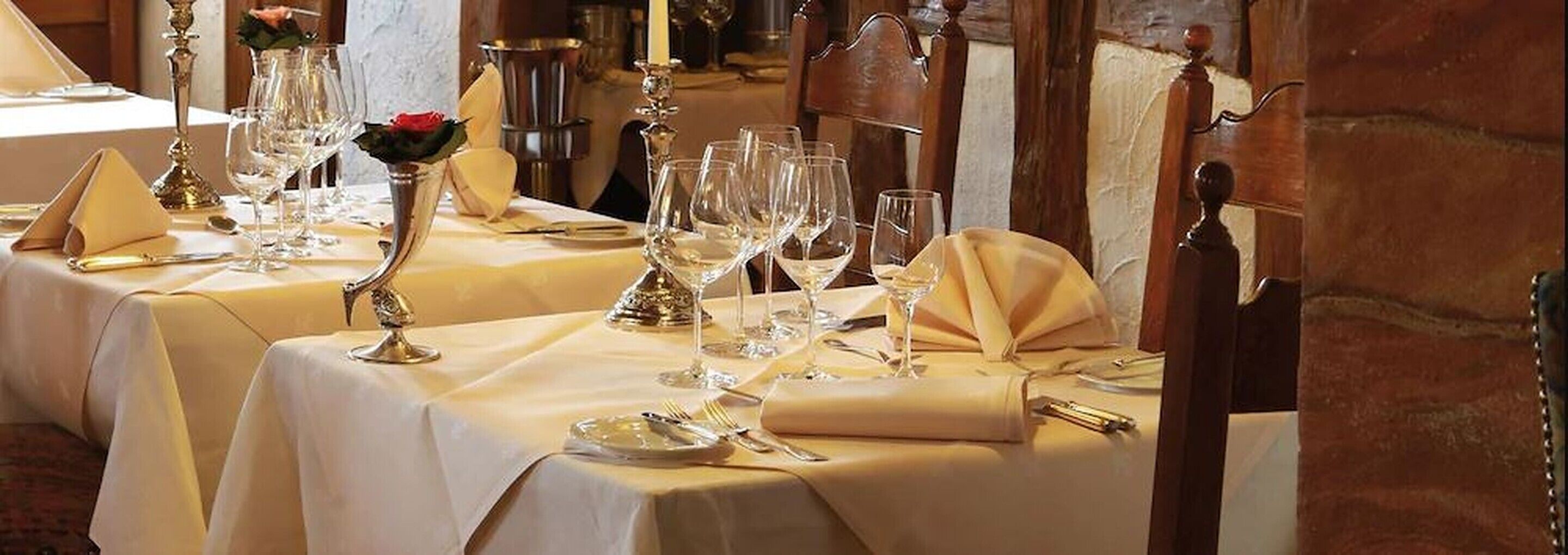 A dining table set with multiple wine glasses, a rose in a vase, and a candle holder.