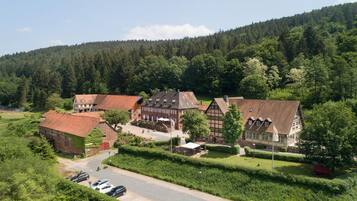A traditional European village with historic buildings, a parking area, and a forested hill in the background.