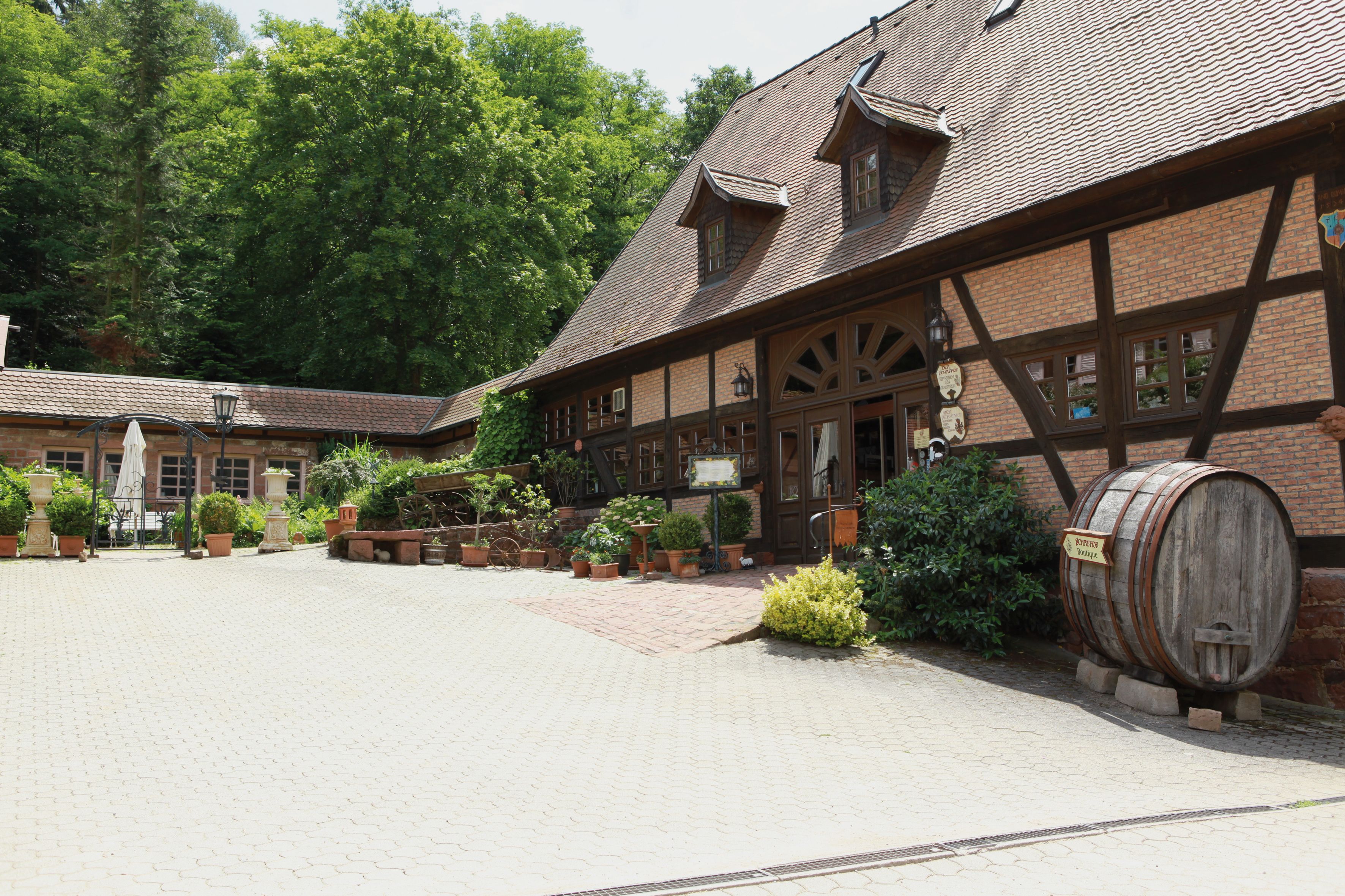 A traditional half-timbered building with a courtyard, potted plants, and a wooden barrel.