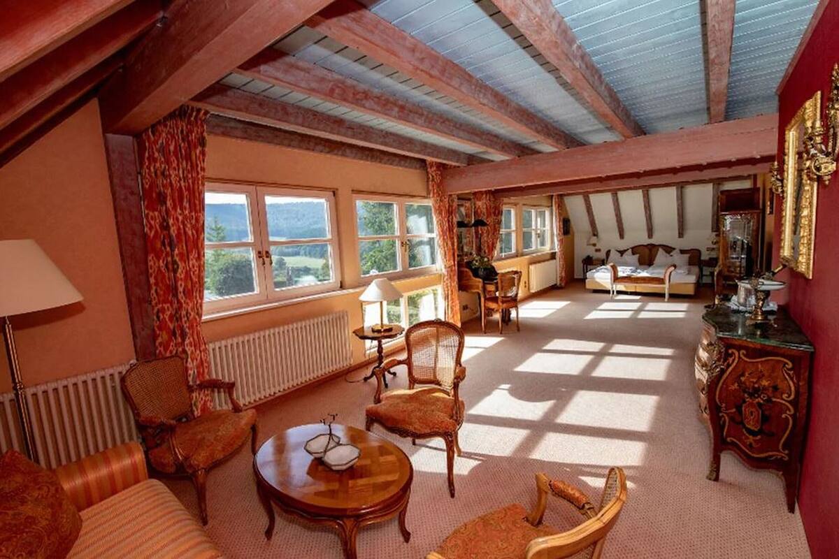 Ein geräumiger Raum mit hohen Decken, großen Fenstern, einem Sofa, einem Esstisch und einem Bett.