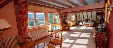 A spacious room with a high ceiling, large windows, a sofa, a dining table, and a bed.