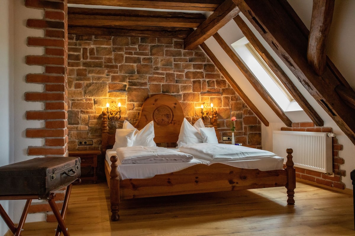 Ein Schlafzimmer mit einem hölzernen Bett, Ziegelwänden und einer schrägen Decke.