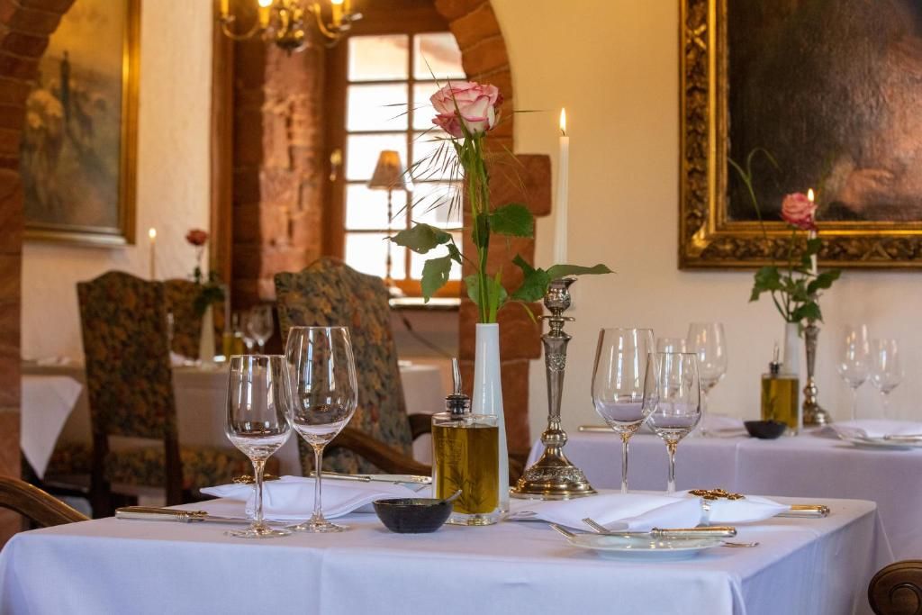 Una mesa de comedor dispuesta con copas de vino, una vela y un florero con una rosa.