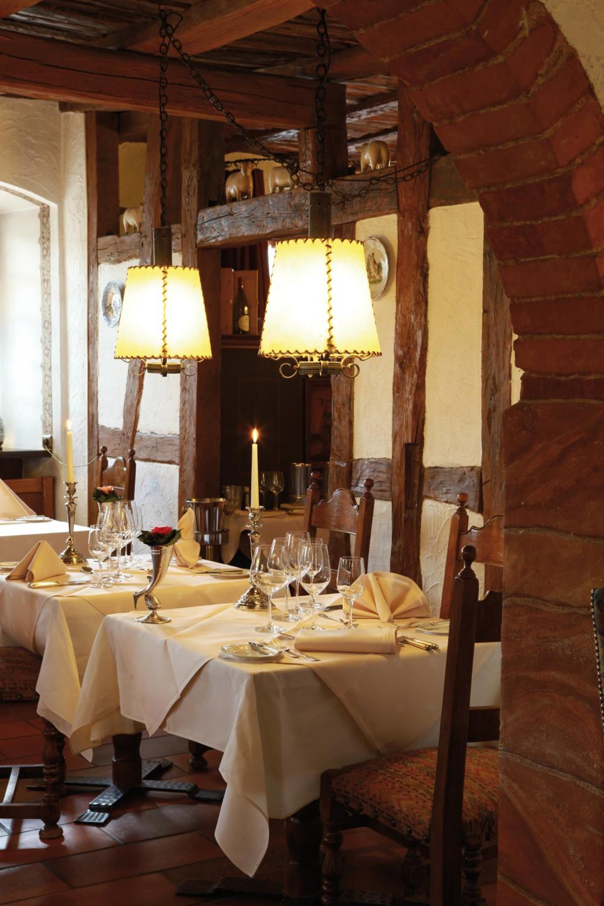 A dining area with tables set for two, featuring white tablecloths, candles, and wine glasses.