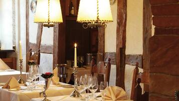 A dining area with tables set for two, featuring white tablecloths, candles, and wine glasses.