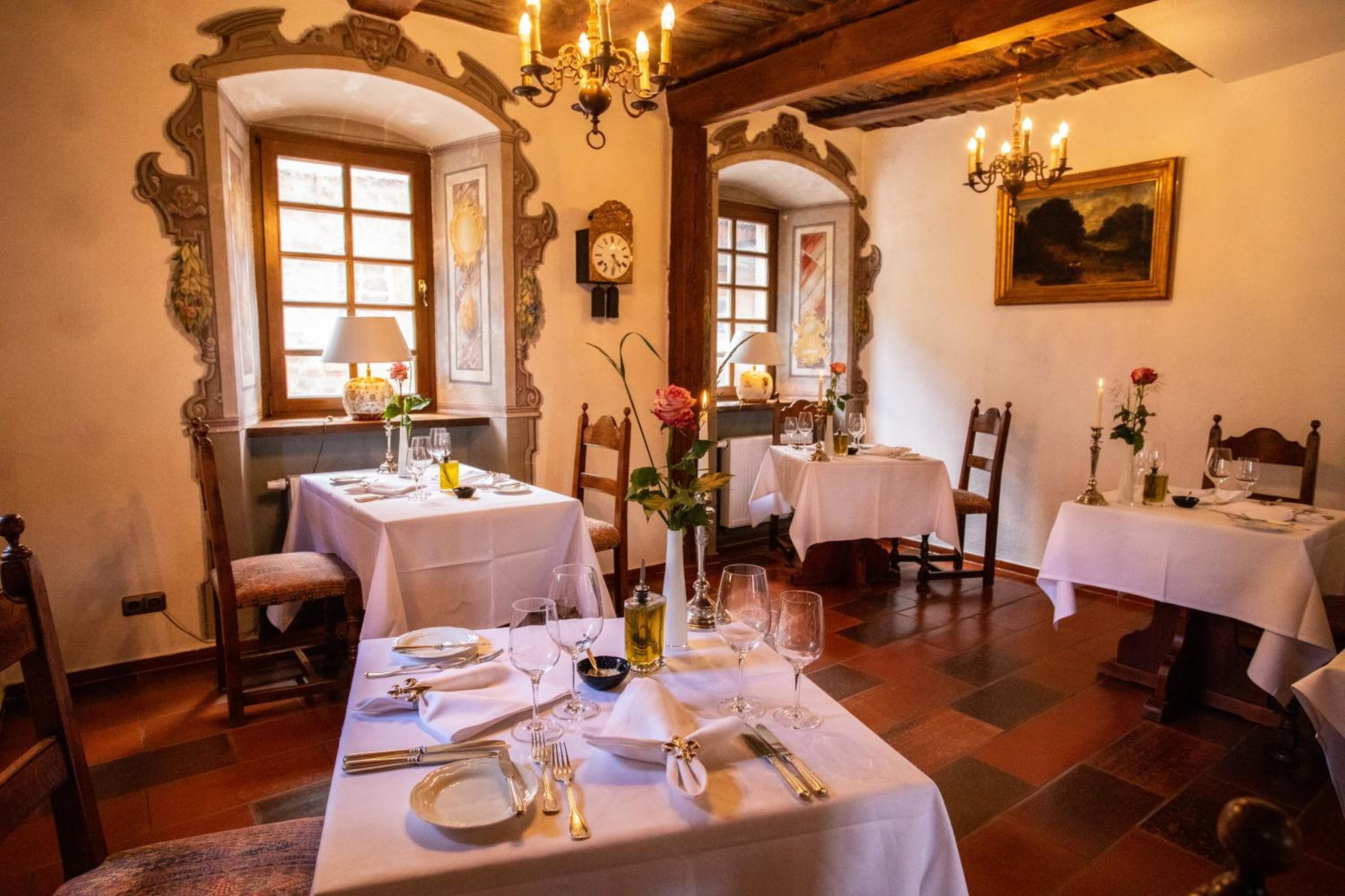 A dining area with tables set for a meal, featuring ornate wall decorations and a chandelier.