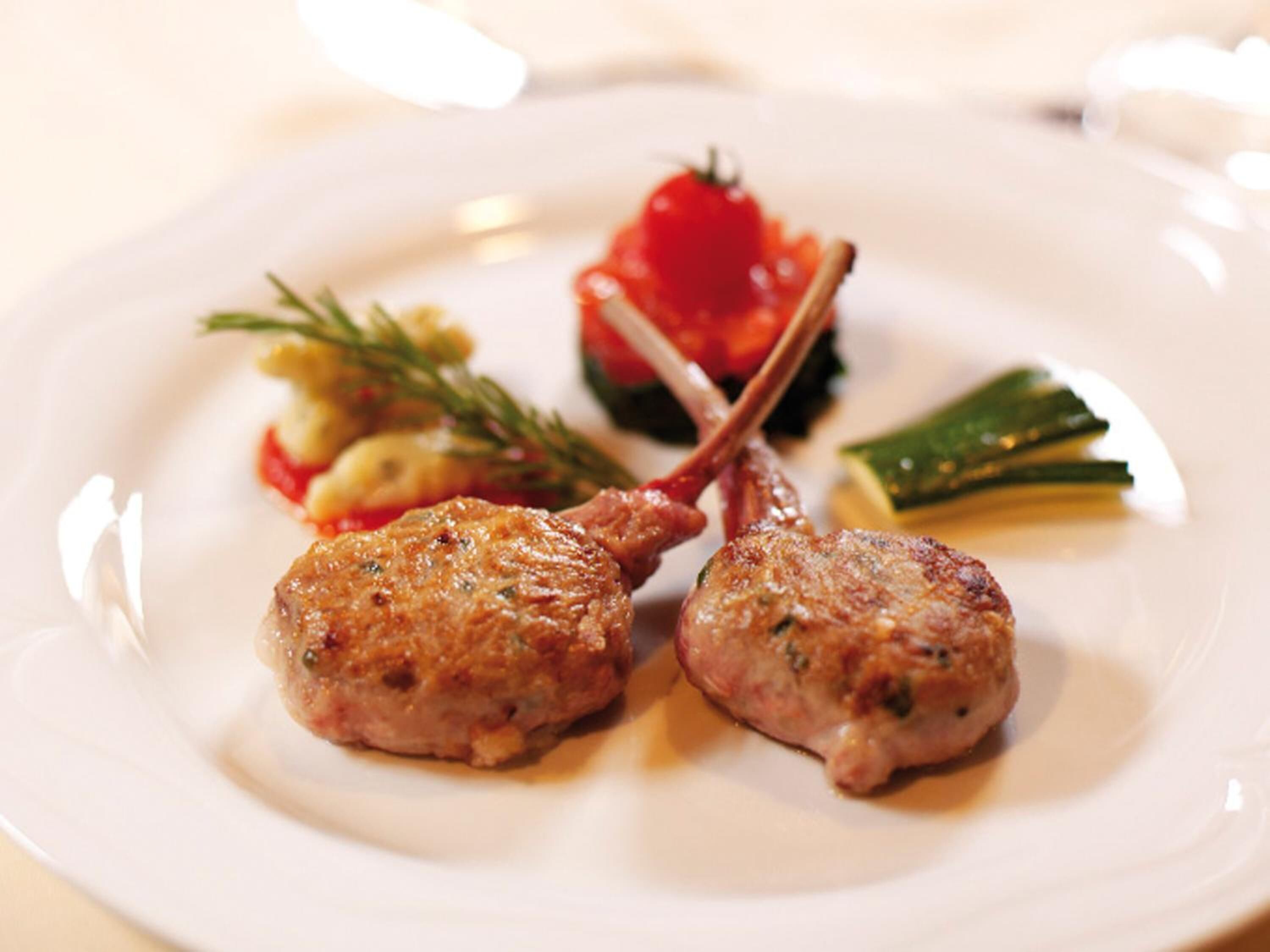 A plate with two grilled lamb chops, a cherry tomato, and some greens.