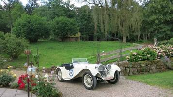 A white convertible car parked on a gravel driveway in a garden setting.