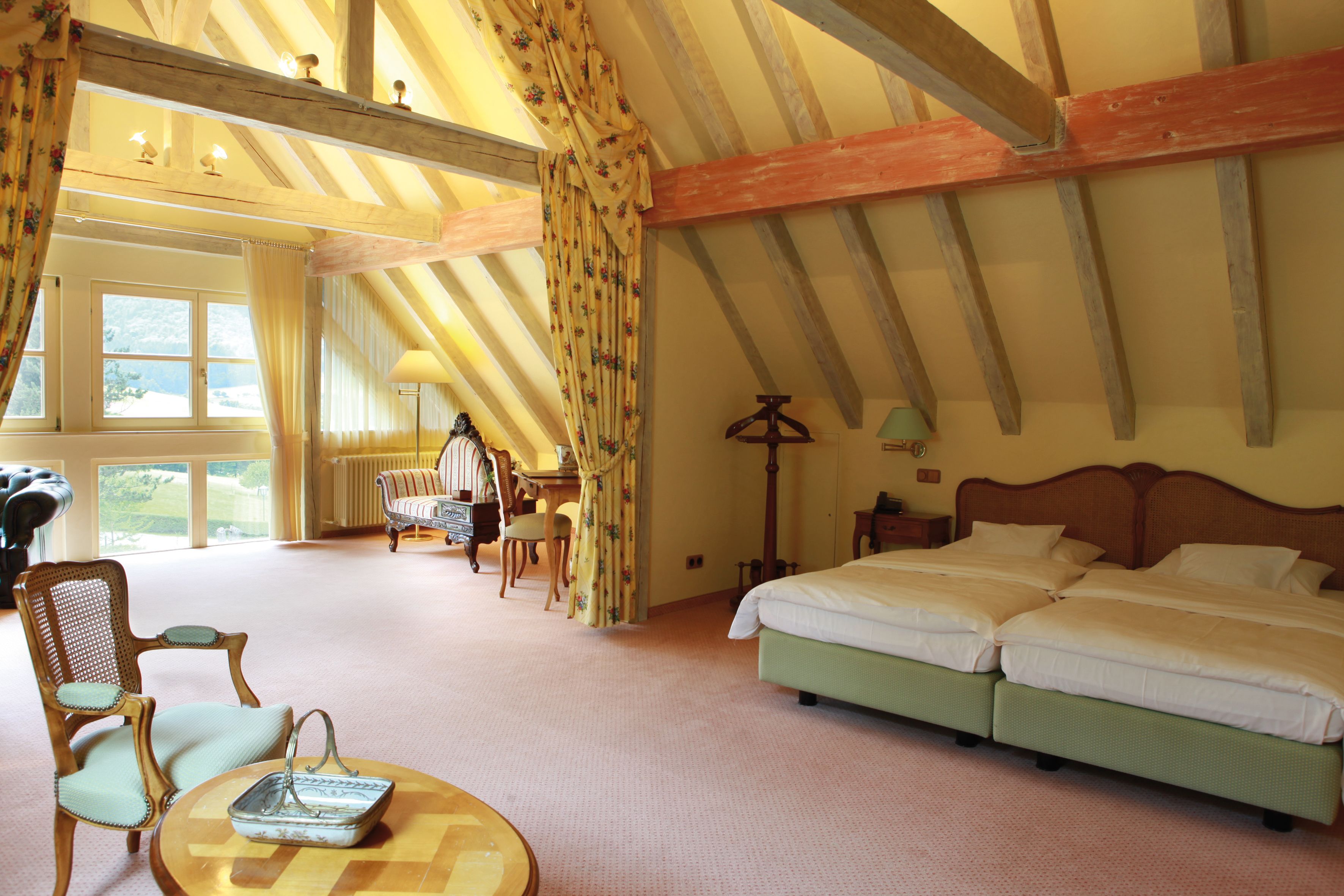 Ein geräumiges Zimmer mit einem großen Bett, einem Sessel, einem Tisch und Blick ins Freie.