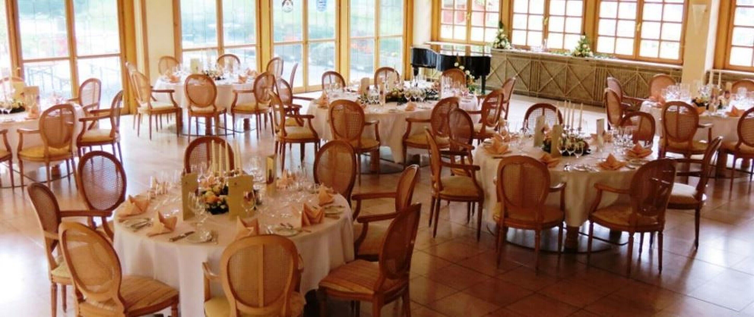 Une salle de banquet avec des tables et des chaises rondes, de grandes fenêtres et une scène.