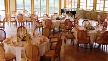 Une salle de banquet avec des tables et des chaises rondes, de grandes fenêtres et une scène.