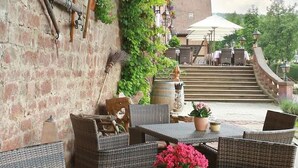 An outdoor patio area with wicker furniture, a stone staircase, and a view of a garden with various plants and flowers. - Hotel Der Schafhof Amorbach (Amorbach)