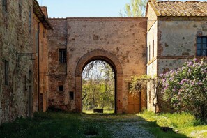 An arched gateway between two buildings, with a rustic stone wall and a wooden door visible through the arch.