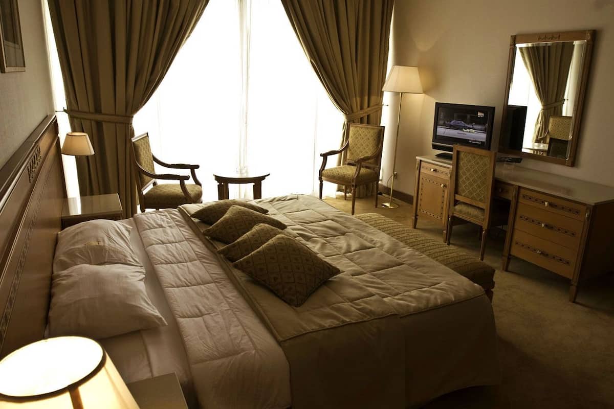 A hotel room with a large bed, two armchairs, a television, and a dresser.