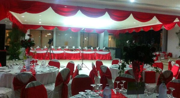 Un salón de banquetes con mesas redondas cubiertas con manteles blancos y cortinas rojas.