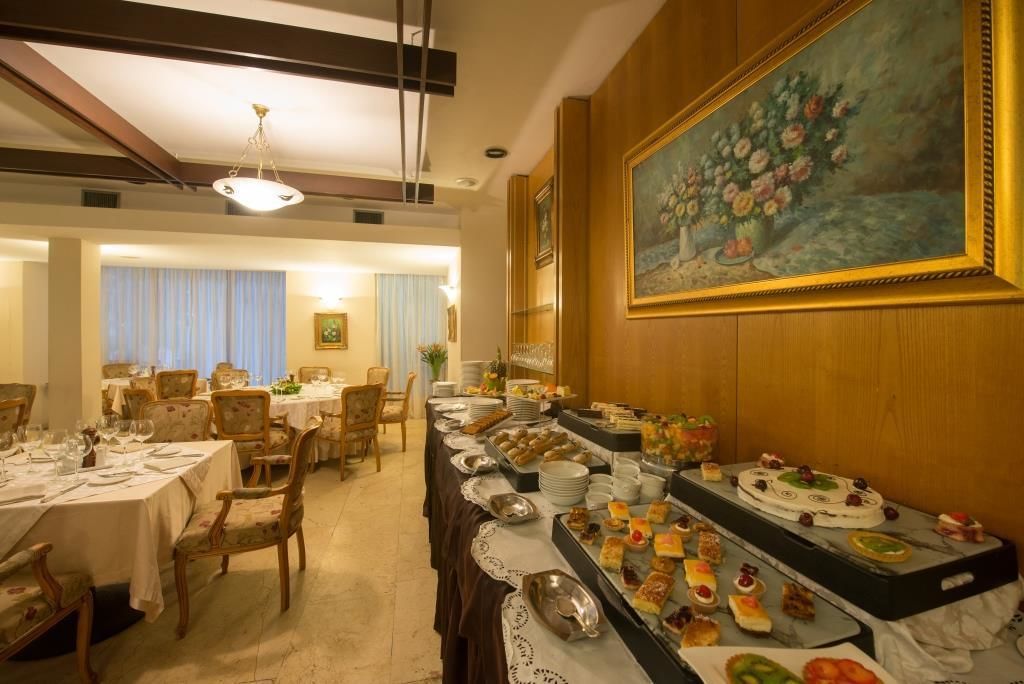 A dining area with tables set for a meal, a buffet with various food items, and a painting on the wall.