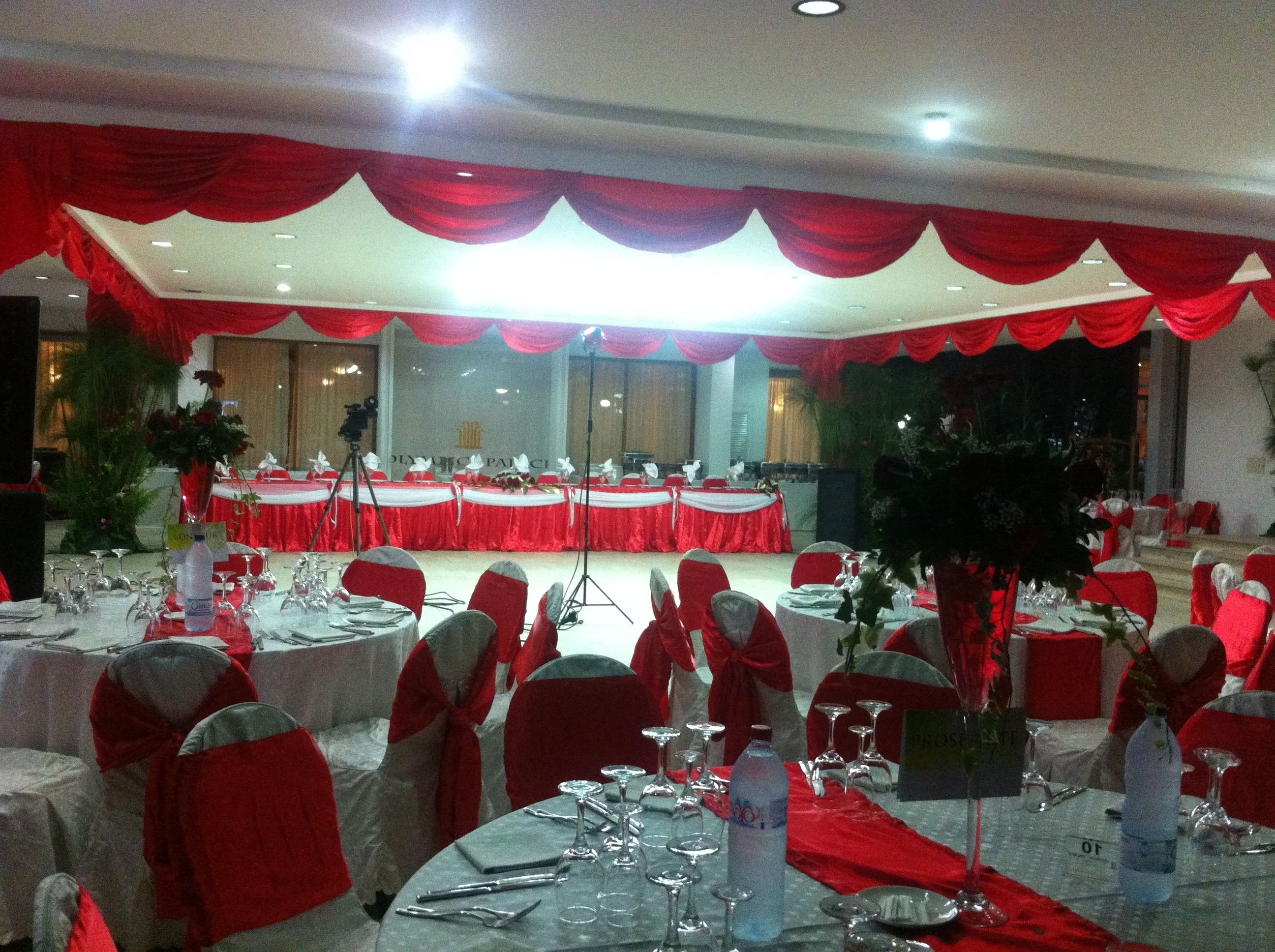 A banquet hall with round tables set for a formal event, adorned with red drapes and white tablecloths.