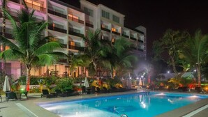 A swimming pool with lounge chairs and palm trees, surrounded by a multi-story building with balconies. - Olympic Palace (Brazzaville)