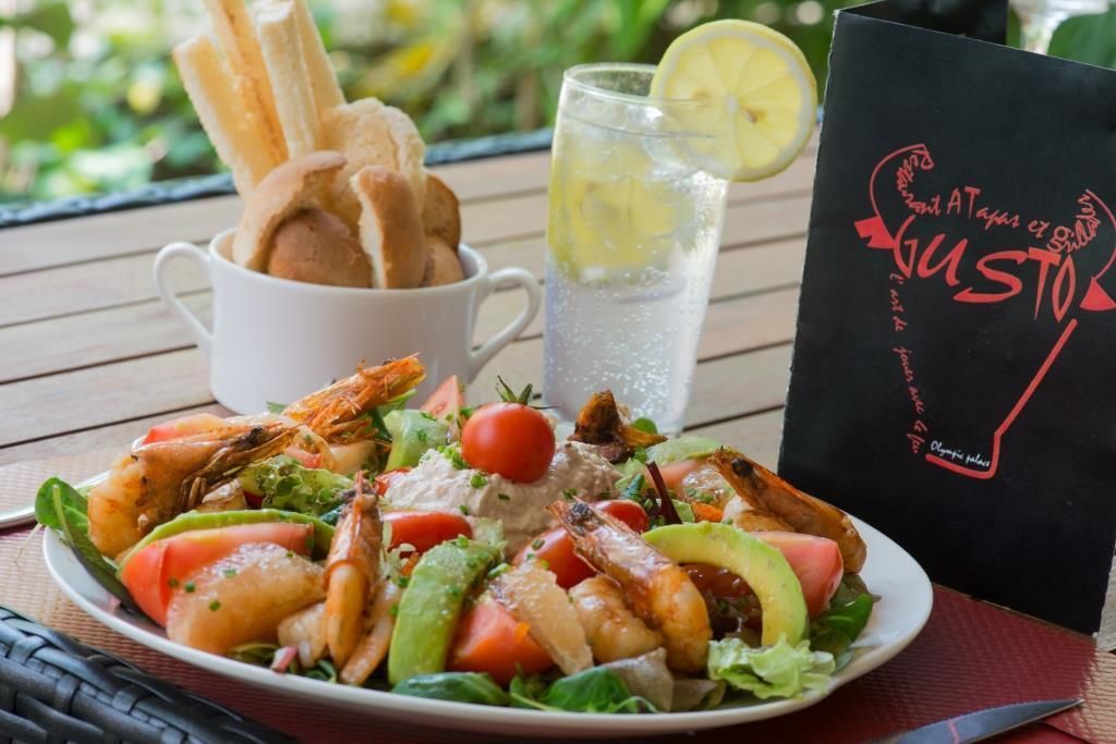 Ensalada de mariscos en un plato, con palitos de pan, un vaso de limonada y una tarjeta de menú sobre una mesa de madera.