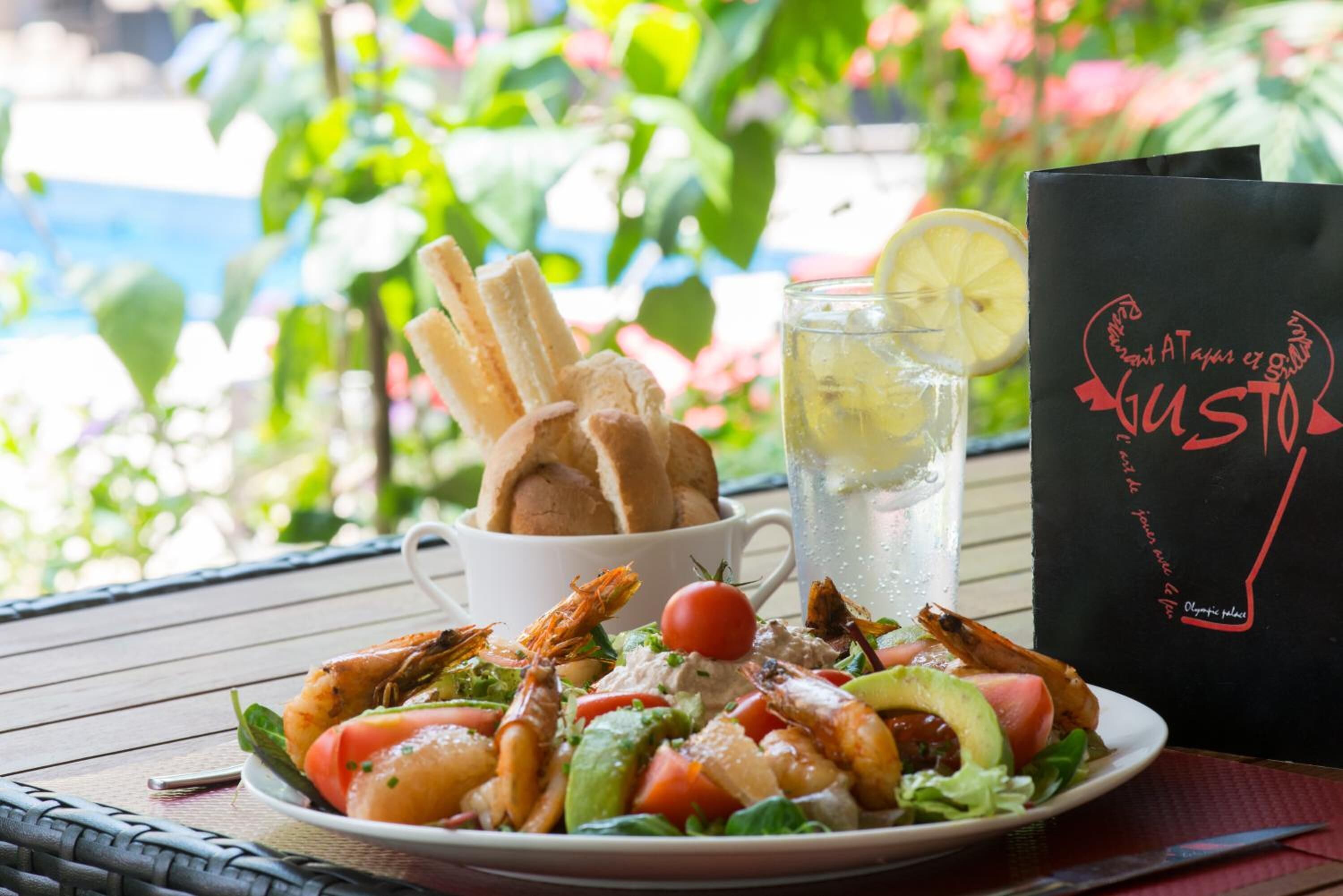 Un plato de ensalada de camarones con palitos de pan, un vaso de bebida helada y un bolso negro con texto rojo.