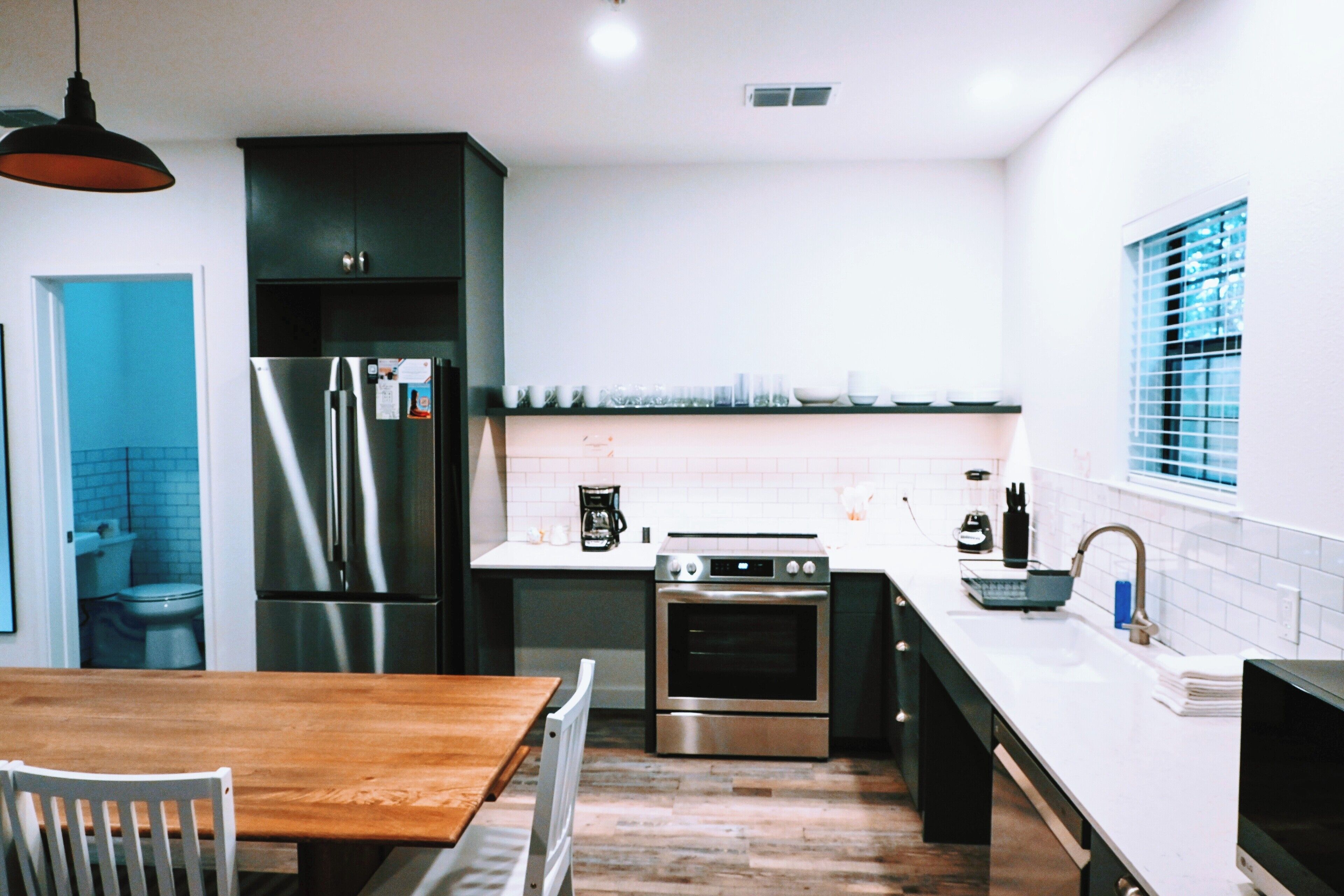 A modern kitchen with stainless steel appliances, a wooden dining table, and a window with blinds.