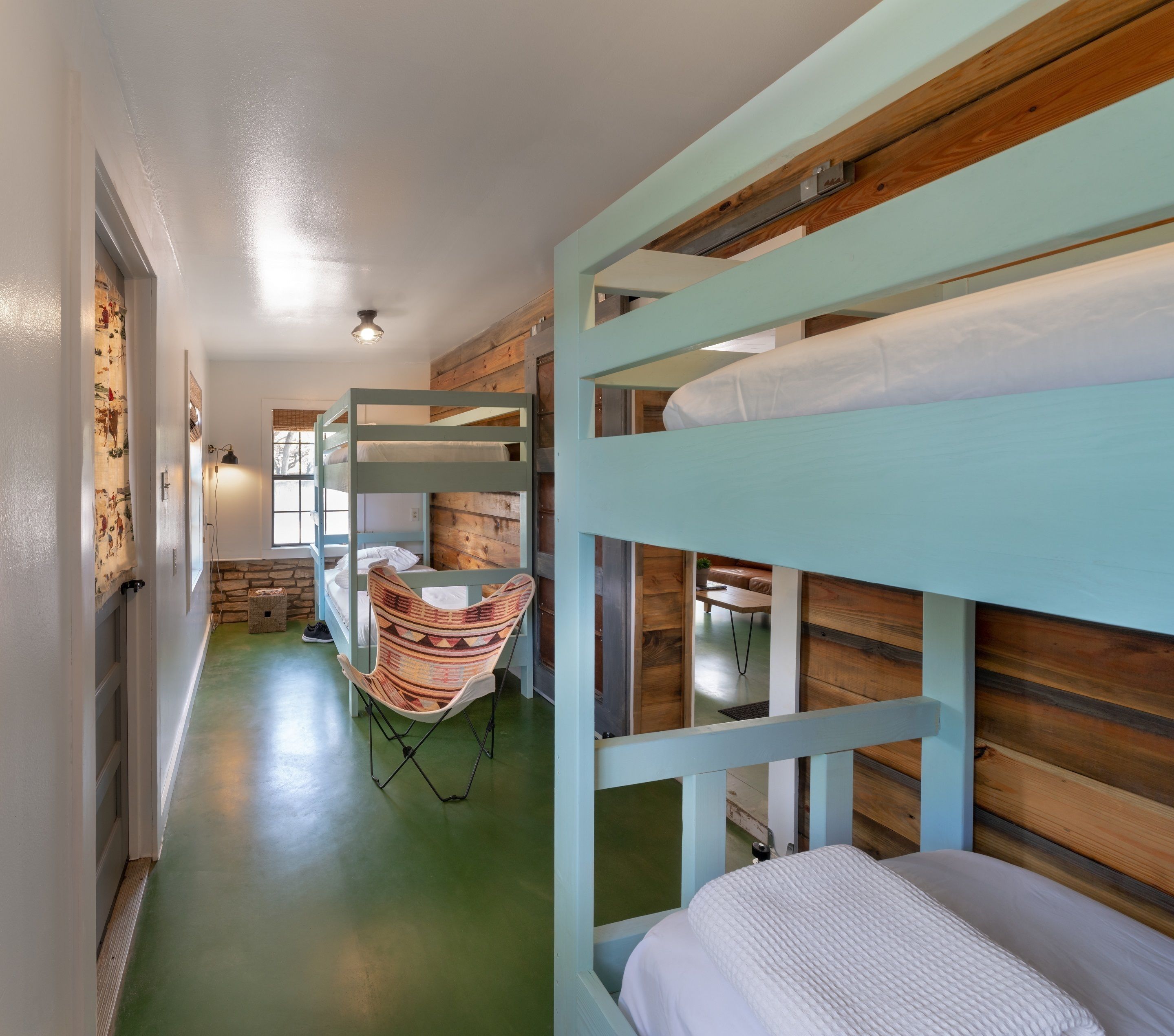 A bunk bed room with a green floor, a woven chair, and a wooden wall.