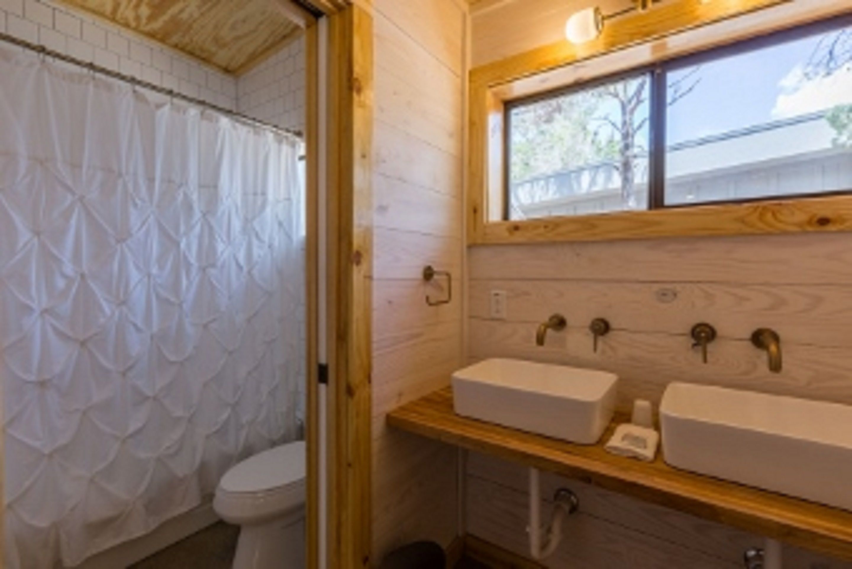 A bathroom with a wooden vanity, two sinks, a shower curtain, and a window.