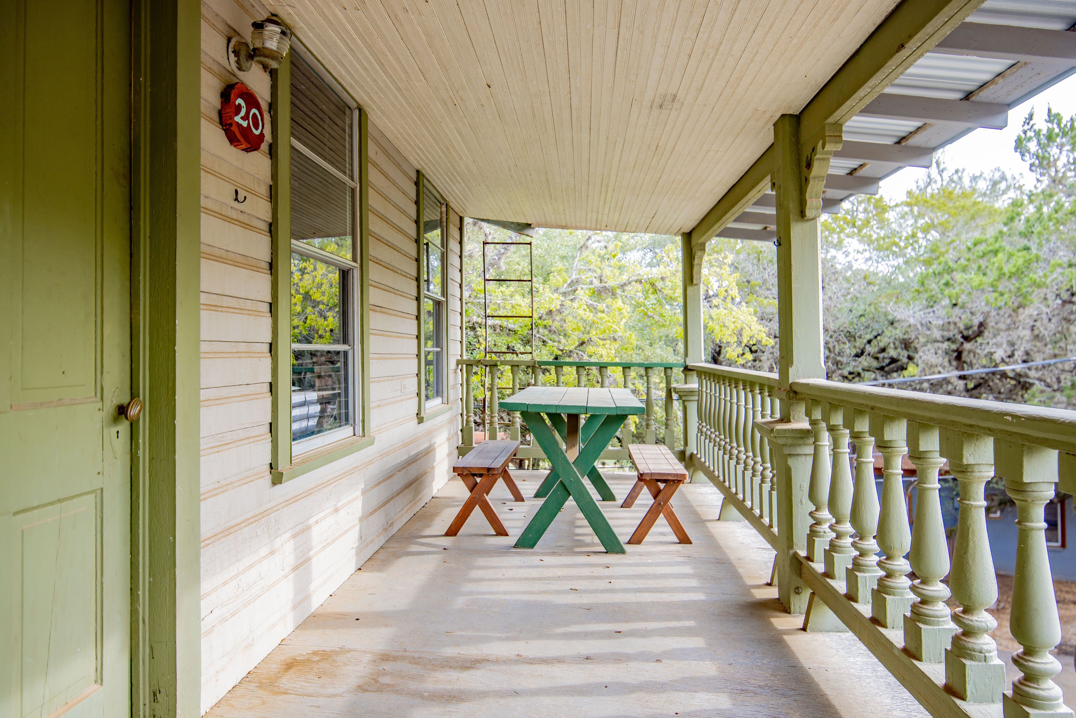 Eine Veranda mit grüner Tür, einem Holztisch und einer Bank.