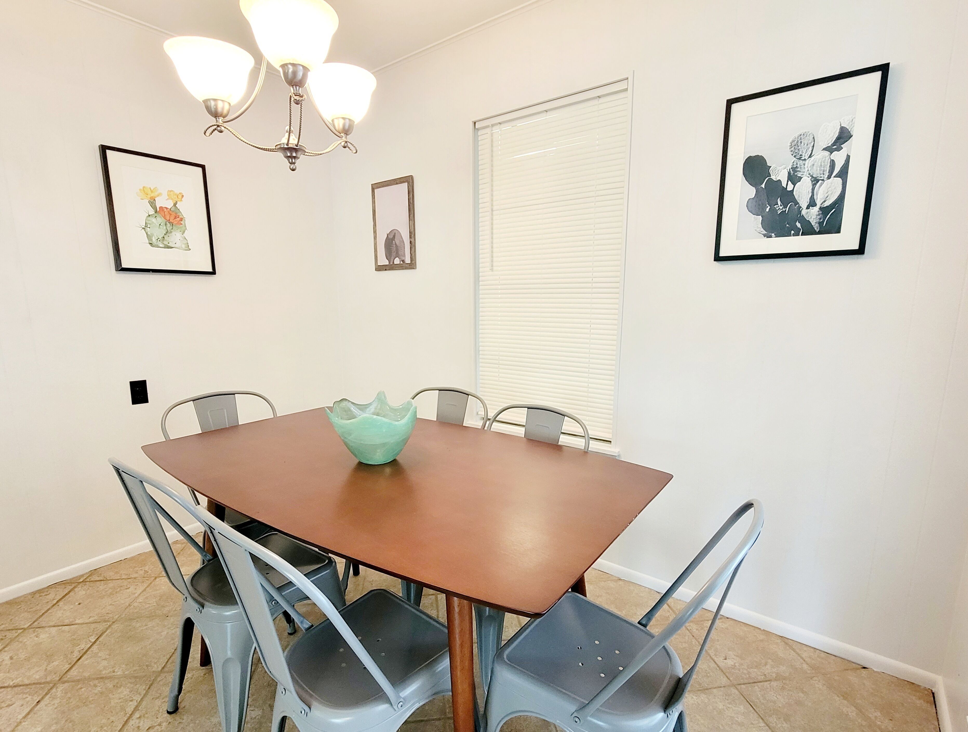 A dining area with a wooden table, metal chairs, a chandelier, and framed artwork on the walls.