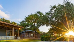 A swimming pool with stone tiles, a covered patio, and a building in the background. - 7A Ranch (Wimberley)