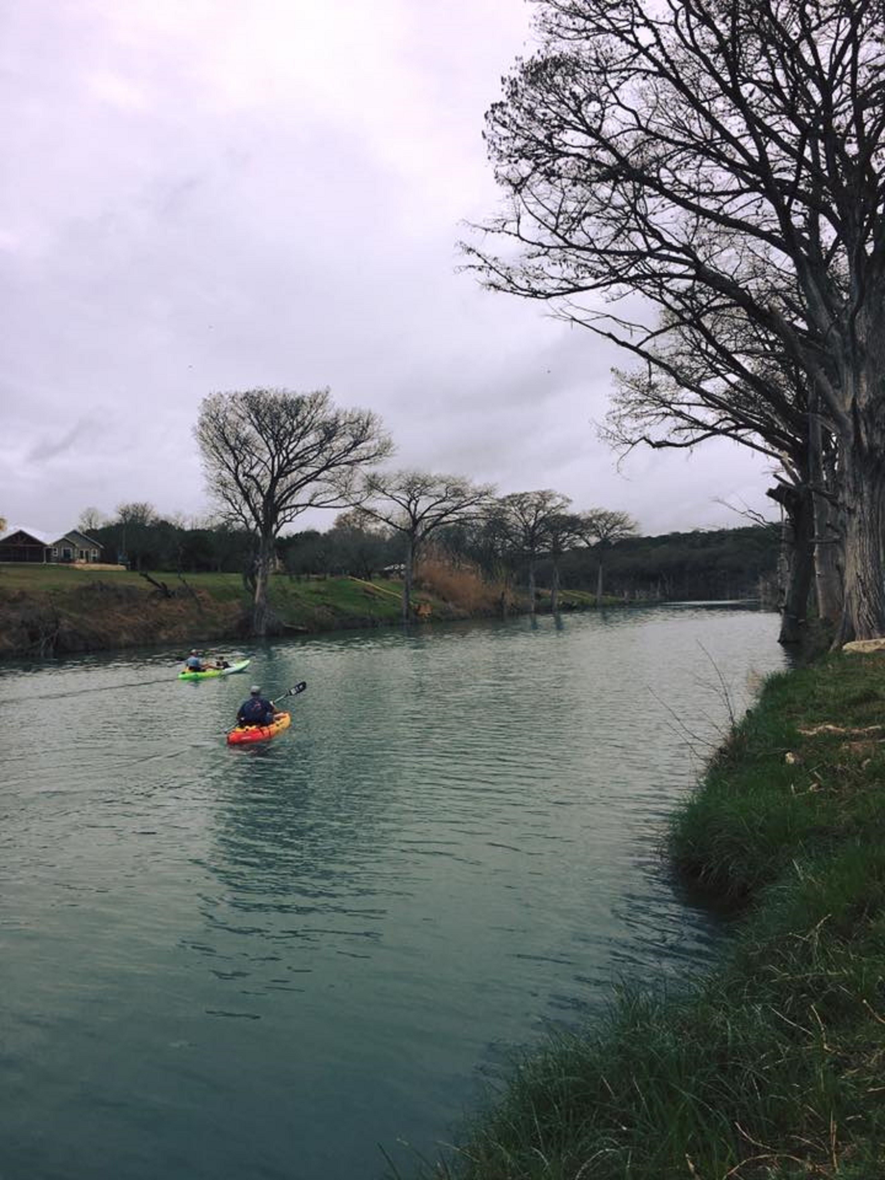 Une rivière paisible où l’on peut faire du kayak, bordée d’arbres et d’une rive herbeuse.