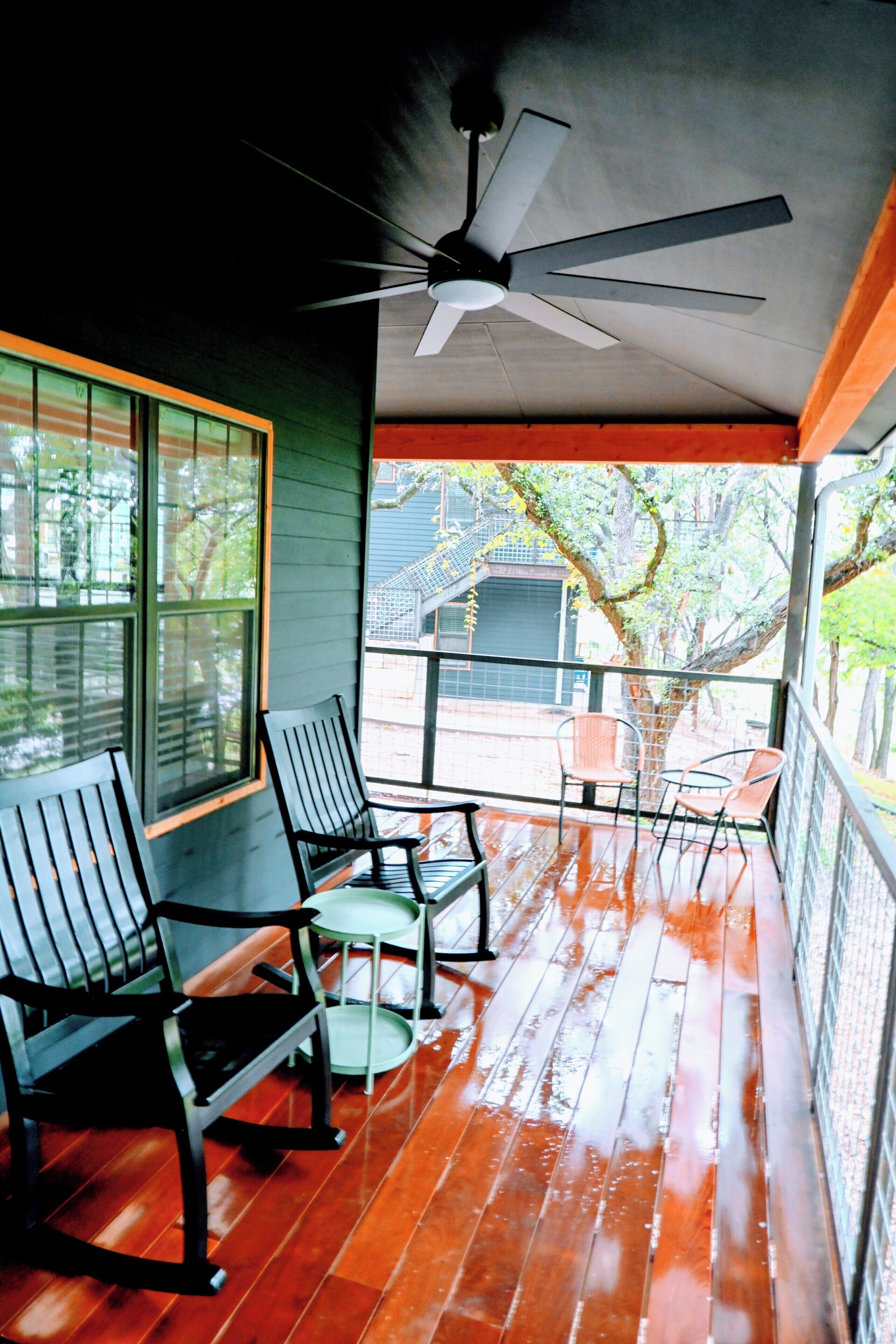 Une terrasse en bois avec des chaises et une table, un ventilateur de plafond et une vue sur l’extérieur.