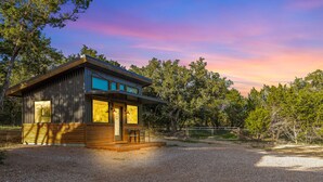 A modern cabin with a wooden exterior, large windows, and a porch area. - 7A Ranch (Wimberley)