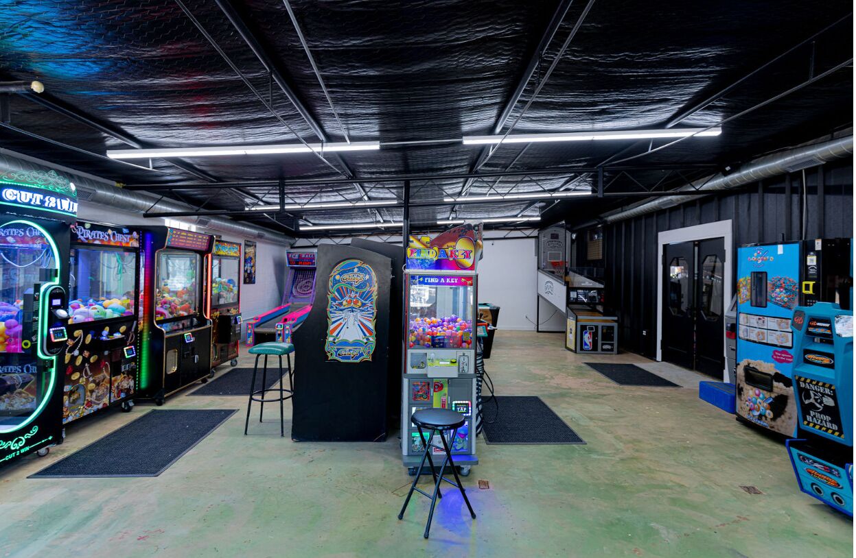 Habitación con juegos de arcade, una máquina expendedora y un taburete pequeño.