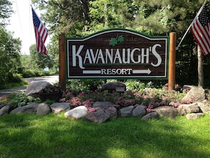 A wooden sign for Kavanaugh's Resort with an arrow pointing right, surrounded by rocks and flowers. - Kavanaugh's Sylvan Lake Resort (Brainerd)
