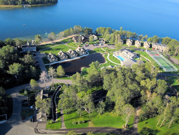 Vista aérea de una propiedad junto al lago con varias casas, cancha de tenis y piscina.